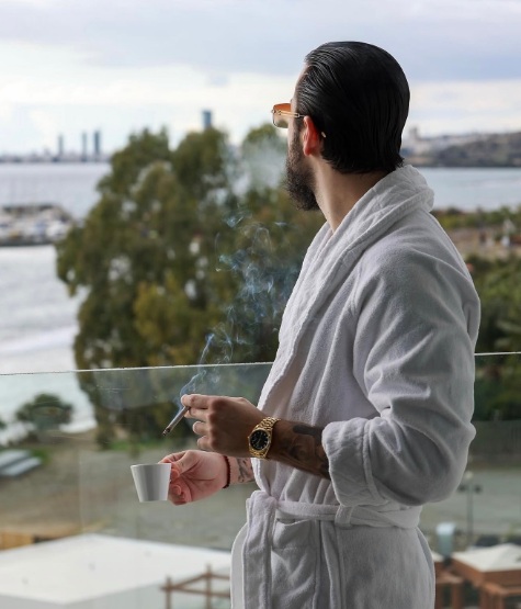 Daniel on a balcony in a robe with a coffee